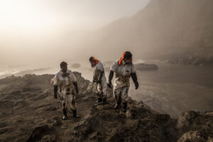 Men in protective suites cleaning up an oil spill, Behind them a foggy mountainous area, photographed by Musuk Nolte, 2022 Challenge Fellow
